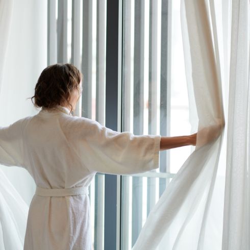 mujer abriendo las cortinas de unas grandes ventanas